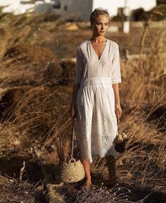 a woman in a white dress is holding a basket and walking through the tall grass