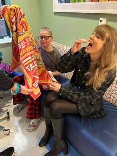 two women sitting on a couch and one is holding a bag of cheetos