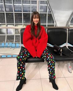 a woman in red sweater and polka dot pants sitting on a bench at an airport