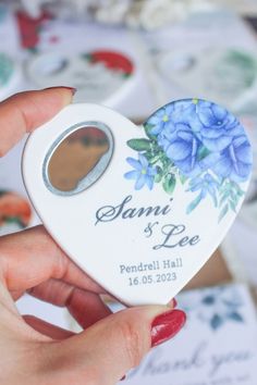 a person holding a small white heart shaped box with blue flowers on the front and side