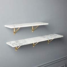 two white marble shelves with gold brackets against a gray wall