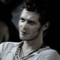 a young man is looking at something while wearing a white shirt and beaded necklace