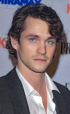 a man with curly hair and blue eyes looks at the camera while wearing a suit