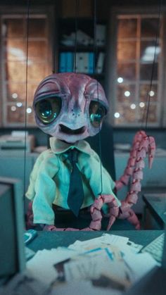 an alien in a tie sitting at a desk