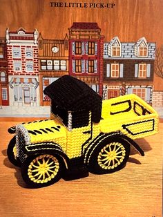 a yellow toy truck with a black hat on it's head and some buildings in the background