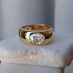 a close up of a gold ring on top of a white marble block with a diamond in the center