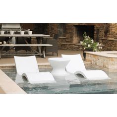 two white chairs sitting on top of a pool next to a stone wall and table