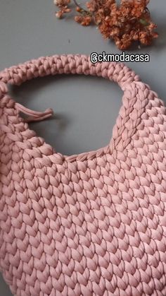 a crocheted pink purse sitting on top of a table next to a flower