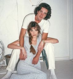 a man and woman sitting on top of a chair with their arms around each other