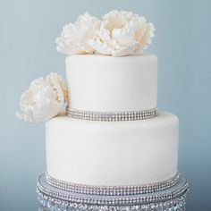 a three tiered wedding cake with white flowers on the top and silver sequins