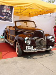 an antique car is on display under a yellow tarp in front of a tent