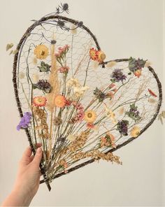 a person holding up a wire heart with dried flowers in the shape of a net