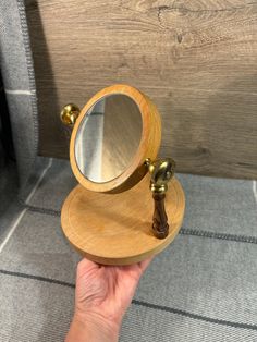 a hand holding a small wooden mirror on top of a table next to a chair