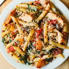 pasta with chicken, spinach and tomato sauce in a white bowl on a wooden table