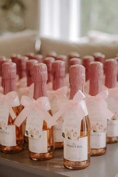 several bottles of wine are lined up on a table with pink bows and tags tied to them