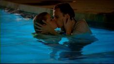 a man and woman kissing in the water near a swimming pool with no one around them