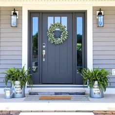 a gray front door with two planters and a wreath on the side of it