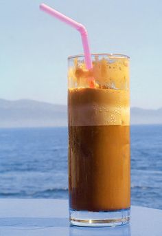 a drink with a straw in it sitting on a table next to the ocean and mountains