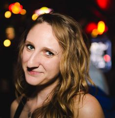 a woman with long hair and blue eyes smiles at the camera in front of bright lights