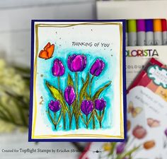 a card with purple flowers and a butterfly on the front, surrounded by crayons