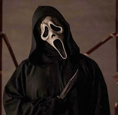 a man in a black hooded jacket with a mask on holding a knife and looking at the camera