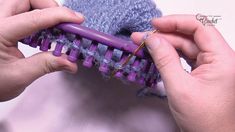 two hands are holding a purple crochet comb with yarn on it and the other hand is knitting