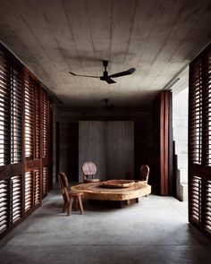 an empty room with two chairs and a round table in the center, surrounded by shutters