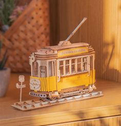 a wooden model of a yellow trolley on a table next to a potted plant