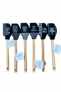 five black and white spatulas are lined up in a row with labels on them