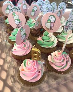 cupcakes with pink, green and white frosting are arranged on a clear tray