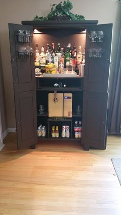 an open cabinet with liquor bottles and glasses on the top, in front of a wooden floor