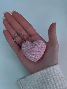 a hand holding a pink heart shaped keychain on it's thumb and ring