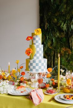 a table topped with a multi layered cake next to candles and flowers in vases