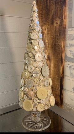 a christmas tree made out of buttons on top of a glass table next to a wooden wall