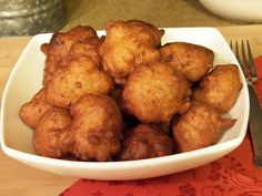 a white bowl filled with tater tots on top of a wooden table next to a fork and knife