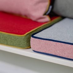 two pillows are sitting on top of each other in front of a white shelf with pink and green cushions