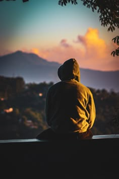 a person sitting on top of a bench looking at the sky and mountains in the distance