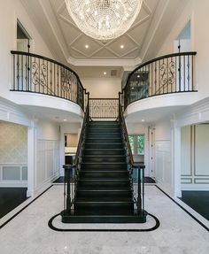 an elegant staircase with chandelier and black railings leads to the second floor