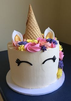 a birthday cake decorated with an unicorn's face and flowers on top is sitting on a table