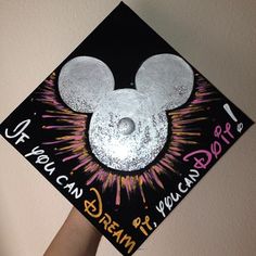 a person is holding up a mickey mouse graduation cap with fireworks in the air on it