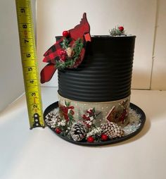 a black hat with pine cones and red berries on it next to a measuring tape