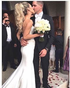 a bride and groom kissing in front of a group of people wearing tuxedos