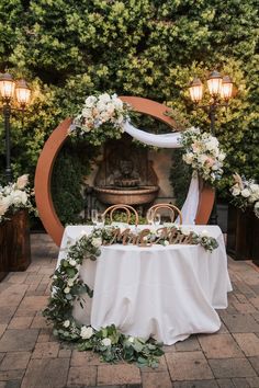 a table with flowers and greenery is set up in front of an archway for a wedding