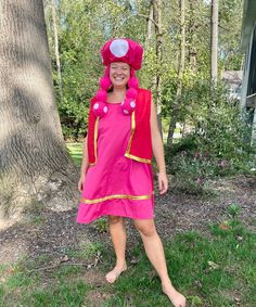 a woman in a pink dress standing next to a tree and smiling at the camera