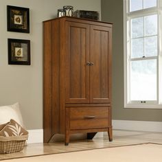 a tall wooden cabinet sitting next to a window in a room with pictures on the wall