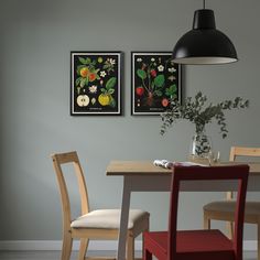 two framed pictures hang on the wall above a dining room table with chairs and a vase filled with flowers