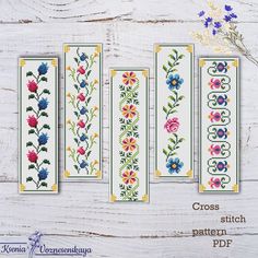 four cross stitch bookmarks with flowers and leaves in them on a white wooden surface