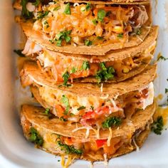 several tortillas stacked on top of each other in a white dish with shredded cheese and toppings