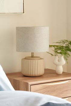 a white vase sitting on top of a wooden table next to a lamp and a bed