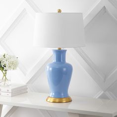 a blue vase sitting on top of a white table next to a lamp and books